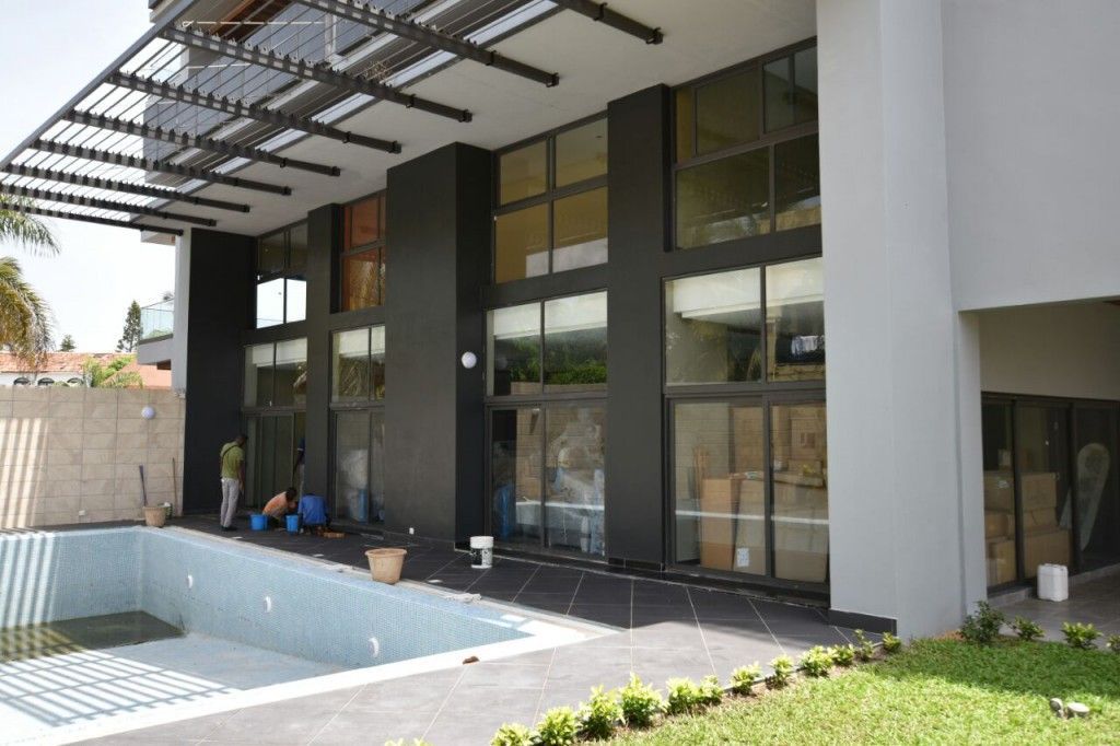 Patio di una casa moderna con porte a vetri, passaggio coperto e una piccola piscina blu accanto al prato.