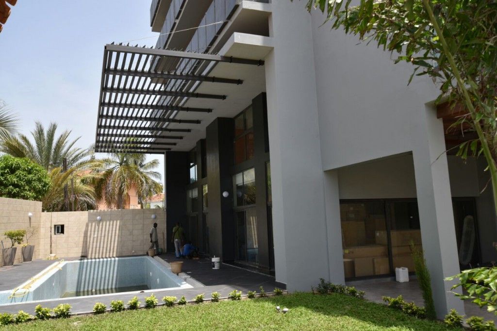 Esterno di una casa moderna con patio coperto, porte a vetri, piscina e prato verde.