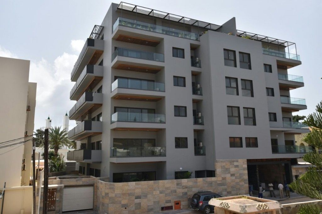 Moderno condominio grigio con balconi e ringhiere sul tetto in un contesto urbano.