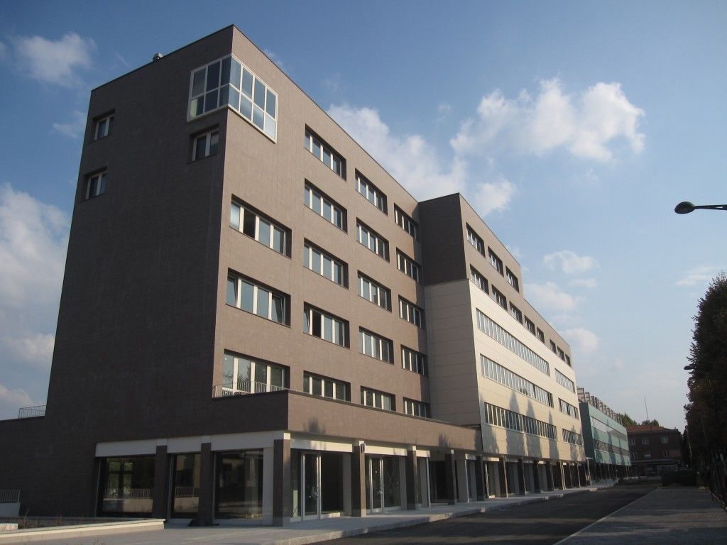 Moderno edificio per uffici a più piani su una strada sotto un cielo parzialmente nuvoloso.