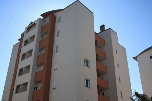 Alto palazzo residenziale con pareti bianche e beige e balconi arancioni contro un cielo azzurro.