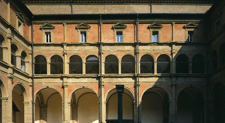 Cortile in mattoni illuminato dal sole con arcate e finestre al piano superiore in un edificio storico
