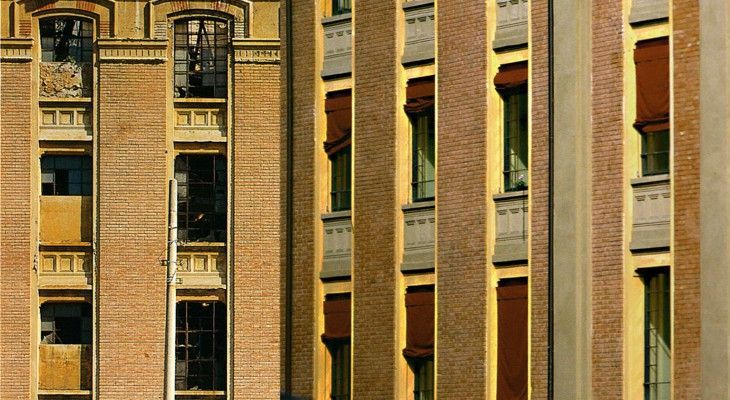 Primo piano della facciata di un edificio in mattoni con finestre strette e tende a rullo rosse e beige.