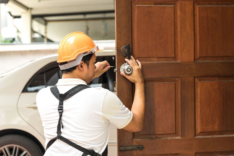 Worker in orange hard hat opening a wooden door with a car in the background