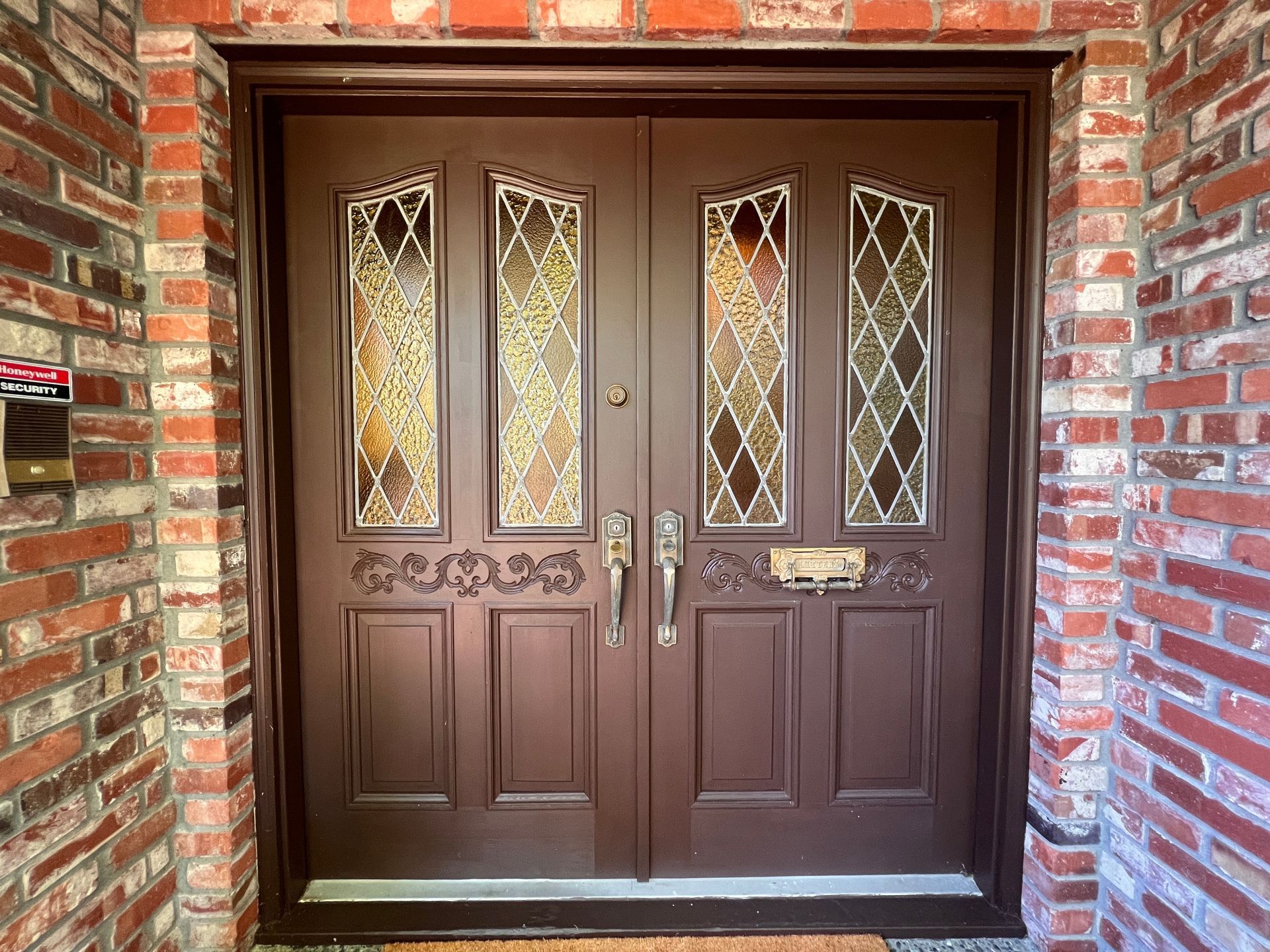 Brown double front door with decorative glass panels in a brick entryway
