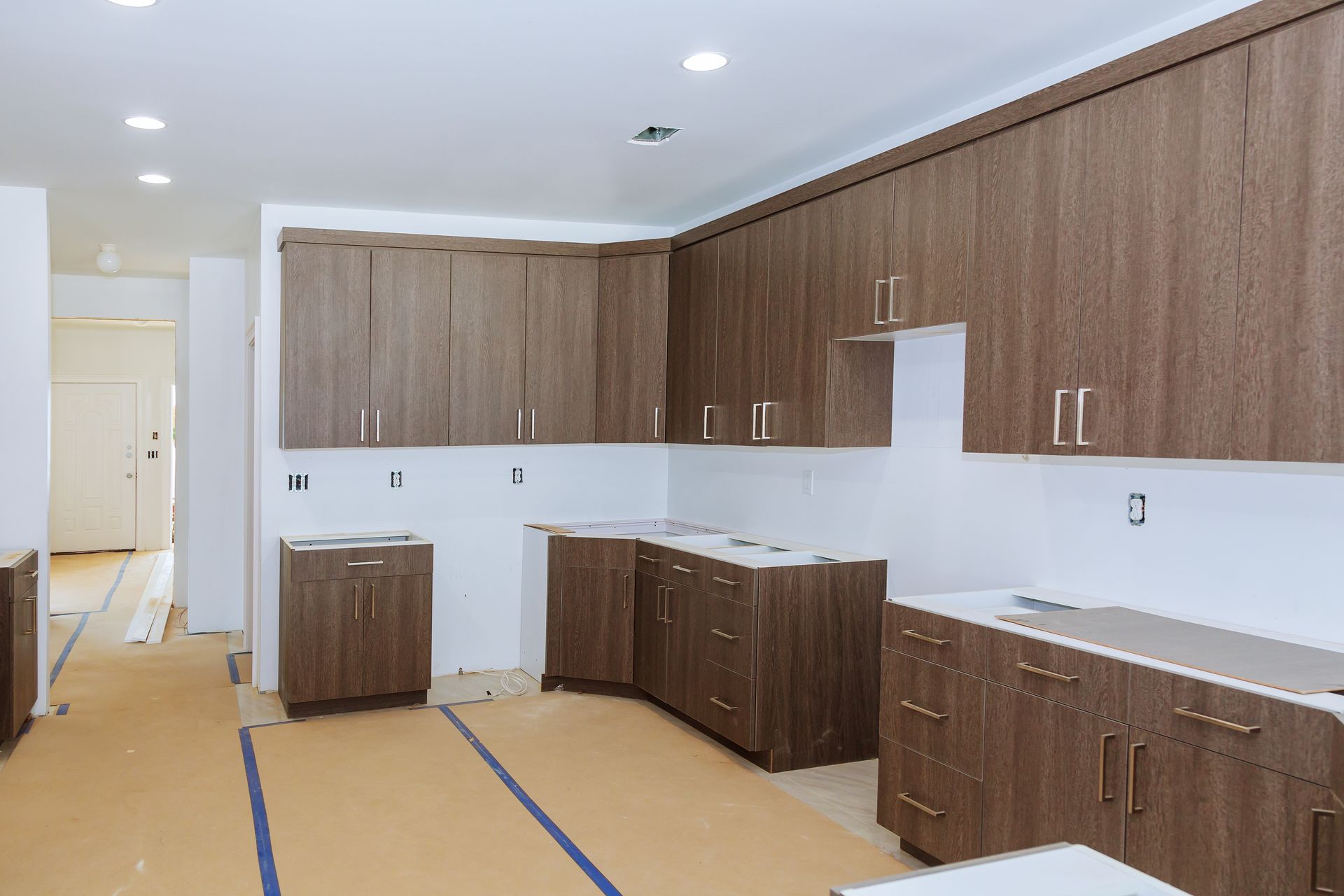 Unfinished kitchen with wood cabinets, white walls, and covered floors during renovation.