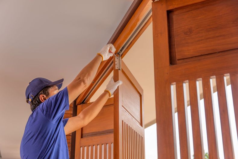 Worker adjusting a wooden door frame indoors with a ladder and tool