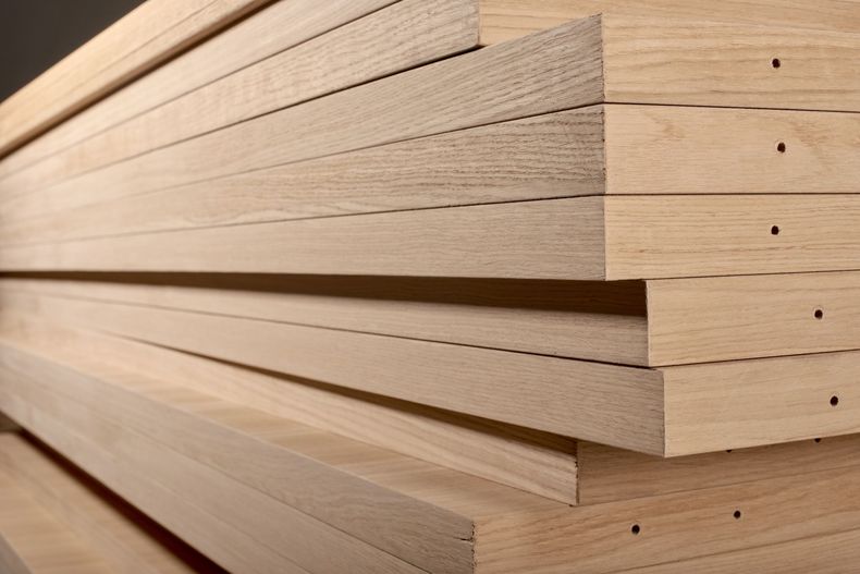 Stacked light wood boards with visible grain and cut ends in a workshop or lumberyard.