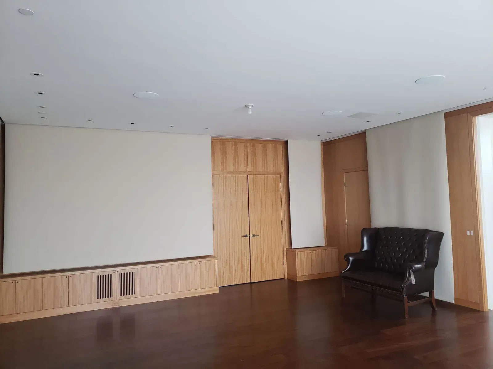 Empty conference room with wood-paneled walls, white ceiling, and a black armchair by the window.