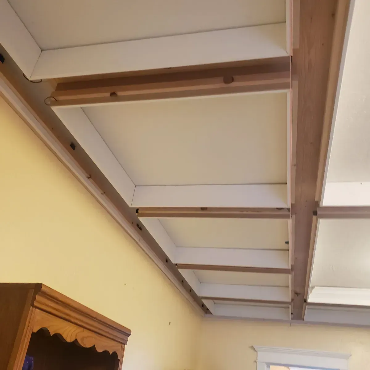 Wooden ceiling beams and white panels above a cream wall in a room