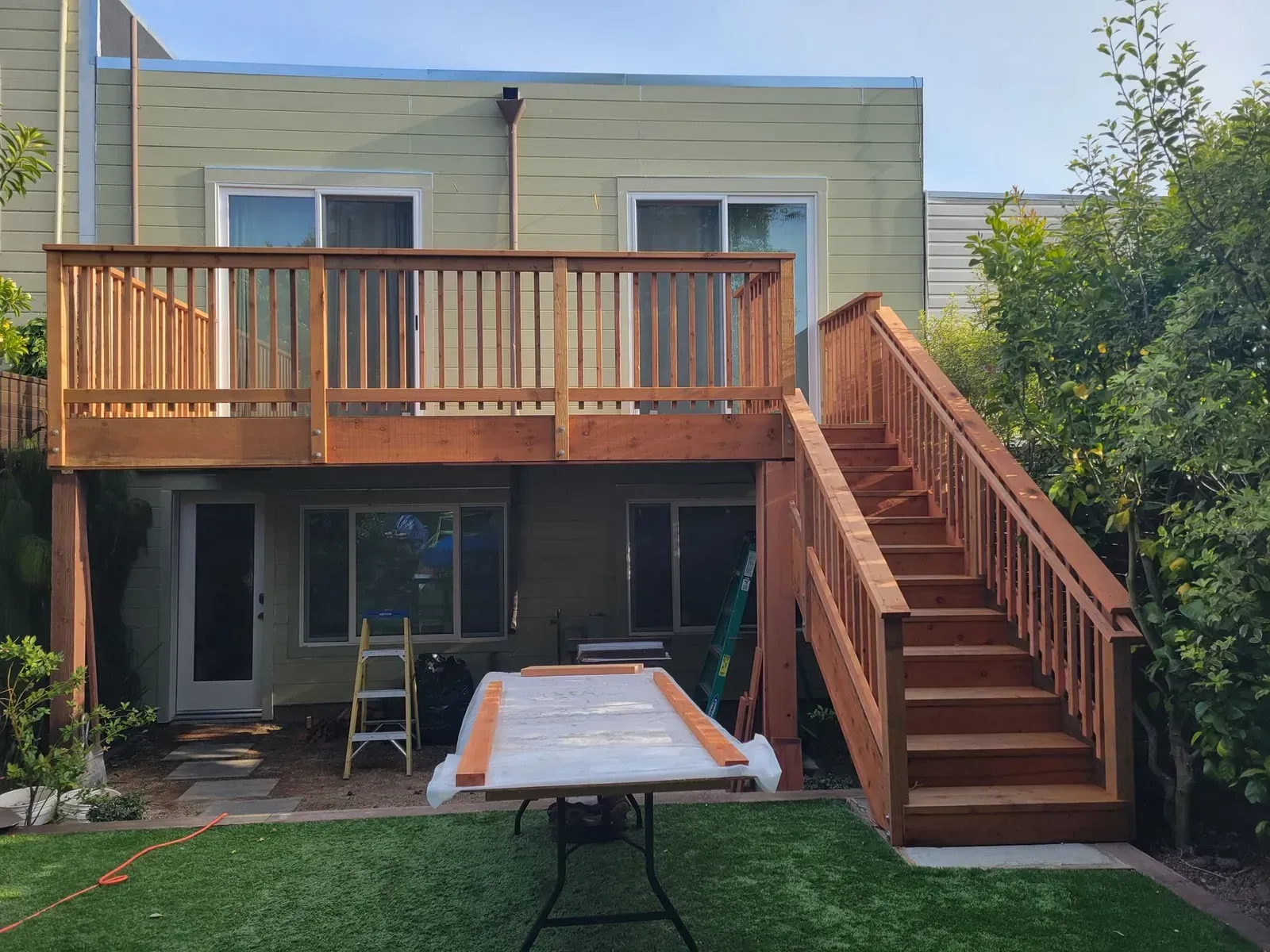 Backyard deck with wooden railing and stairs above a patio, with a folding table in front