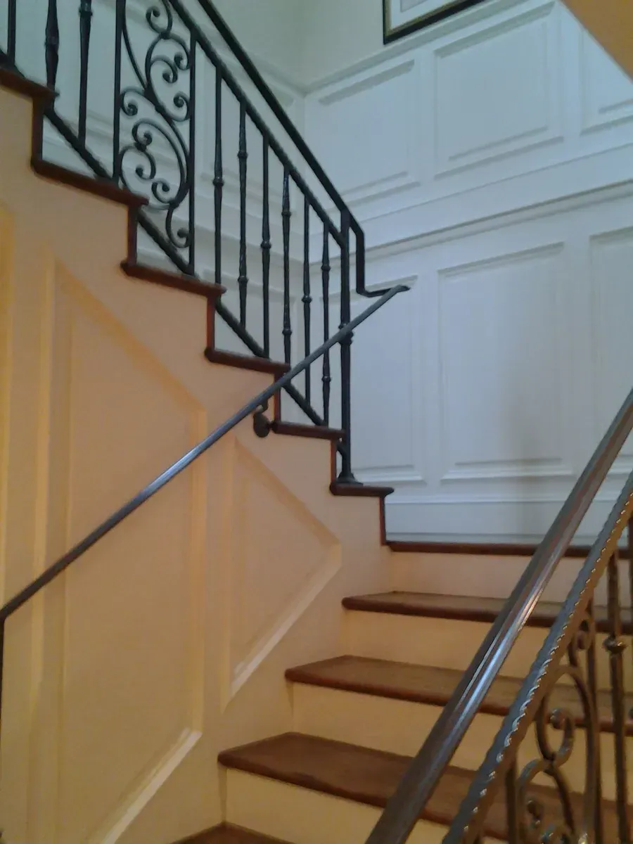 Indoor staircase with wooden steps, white paneled walls, and black wrought-iron railing