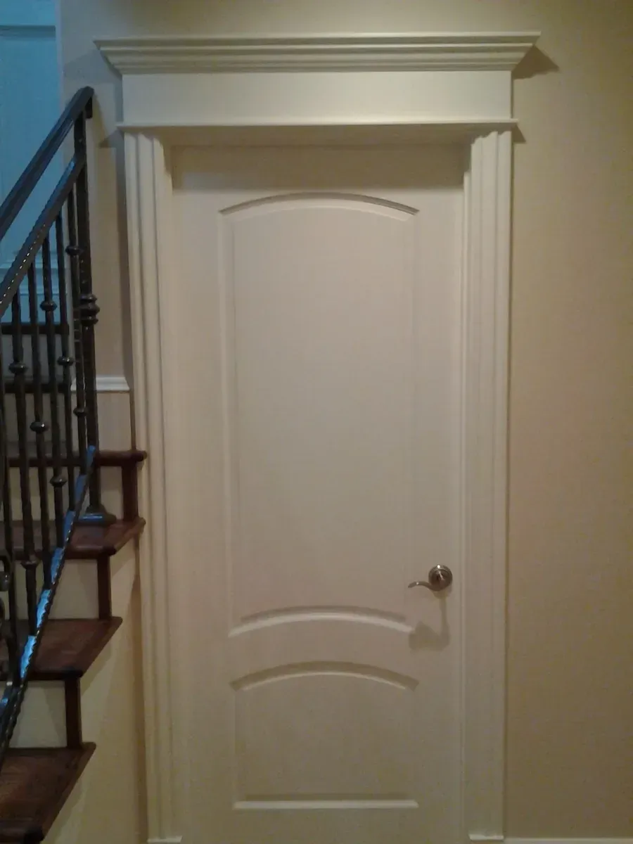 White interior door with arched trim beside a staircase in a home hallway