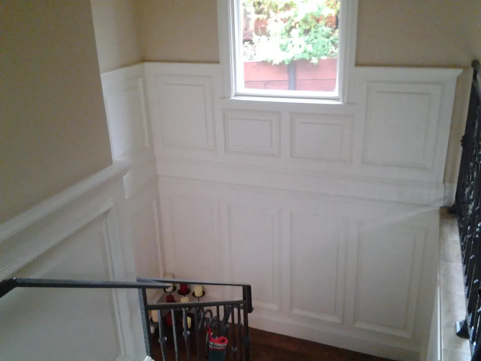 Stair landing with white wainscoting, a small window, and a black handrail beside the stairs