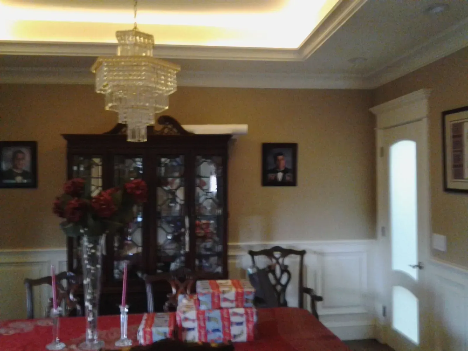 Dining room with chandelier, china cabinet, table centerpiece, and wrapped gifts near a window