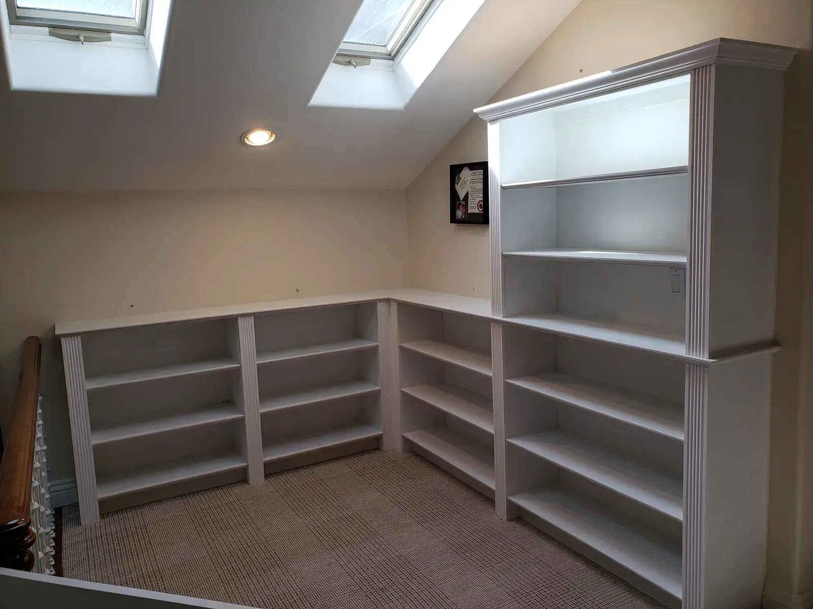 Small attic room with gray built-in shelves under skylights and a patterned carpet.