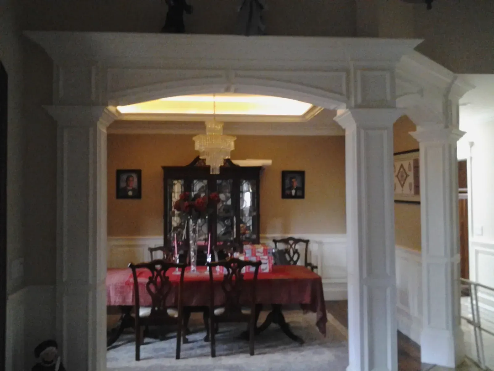 Formal dining room with a chandelier, white columns, and a table draped in red cloth.