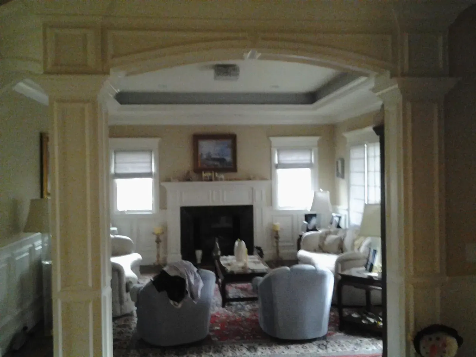 Elegant living room with white fireplace, gray chairs, and a patterned rug in a bright bay window setting