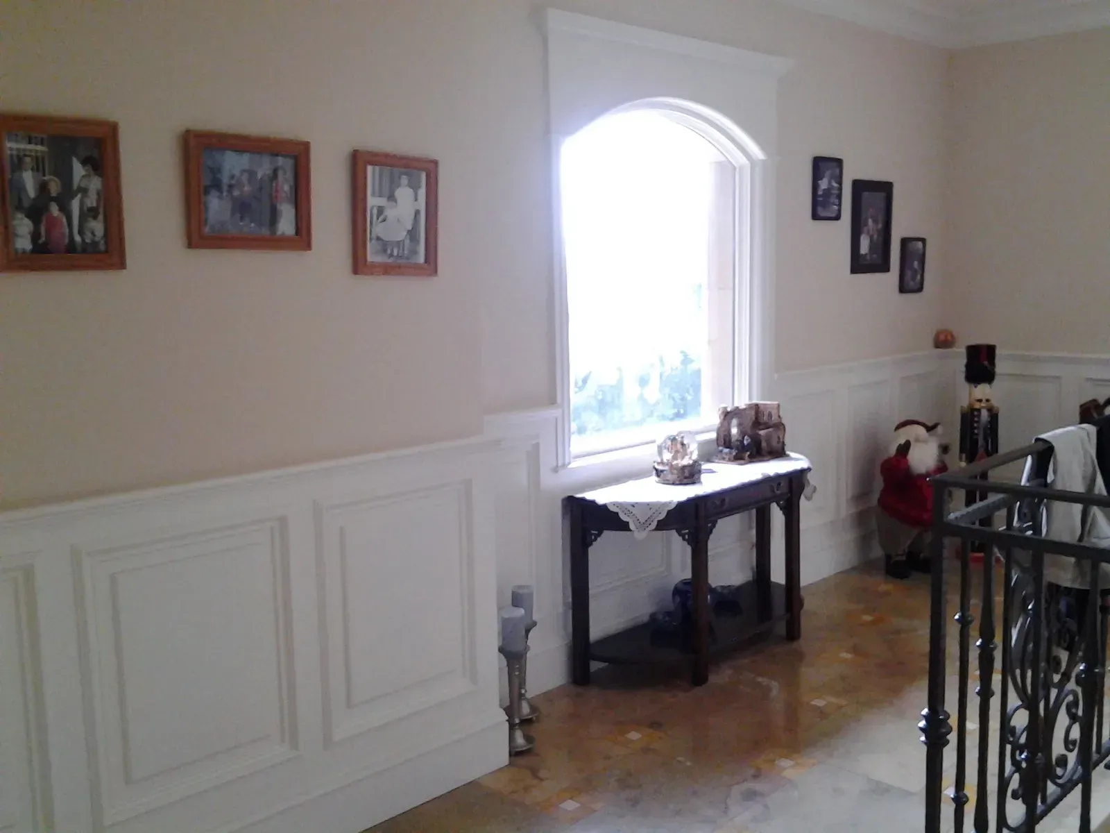 Hallway with framed photos, white wainscoting, arched window, and a small table by the wall.