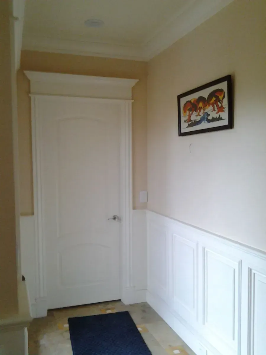 Narrow hallway with white wainscoting, a closed white door, and a small framed picture on the wall.