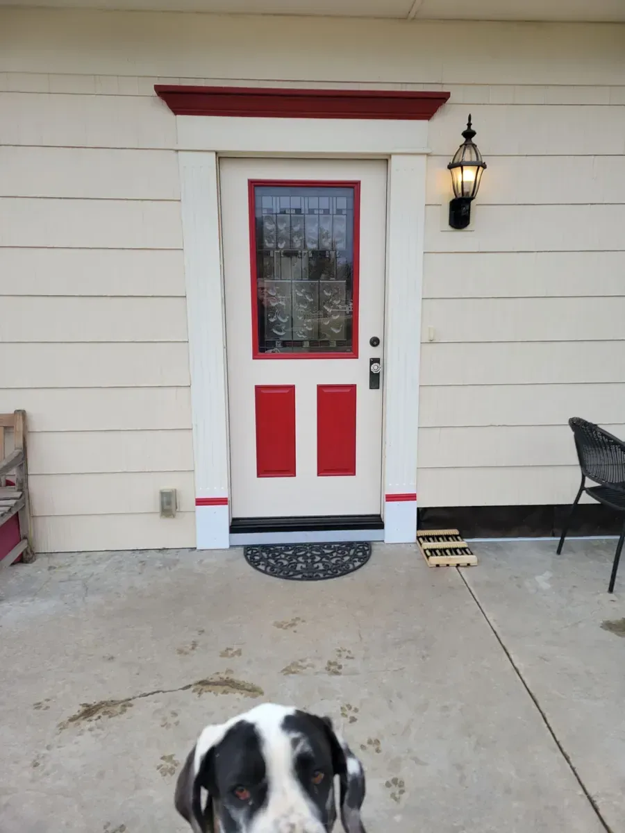 Front door with red trim and a wall lantern; a black-and-white dog is partly visible at the bottom.
