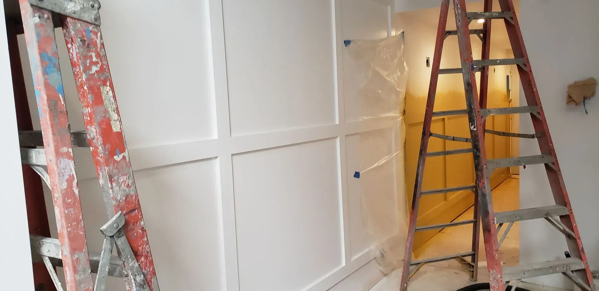 Painted wall panels being installed in a room, with ladders on both sides