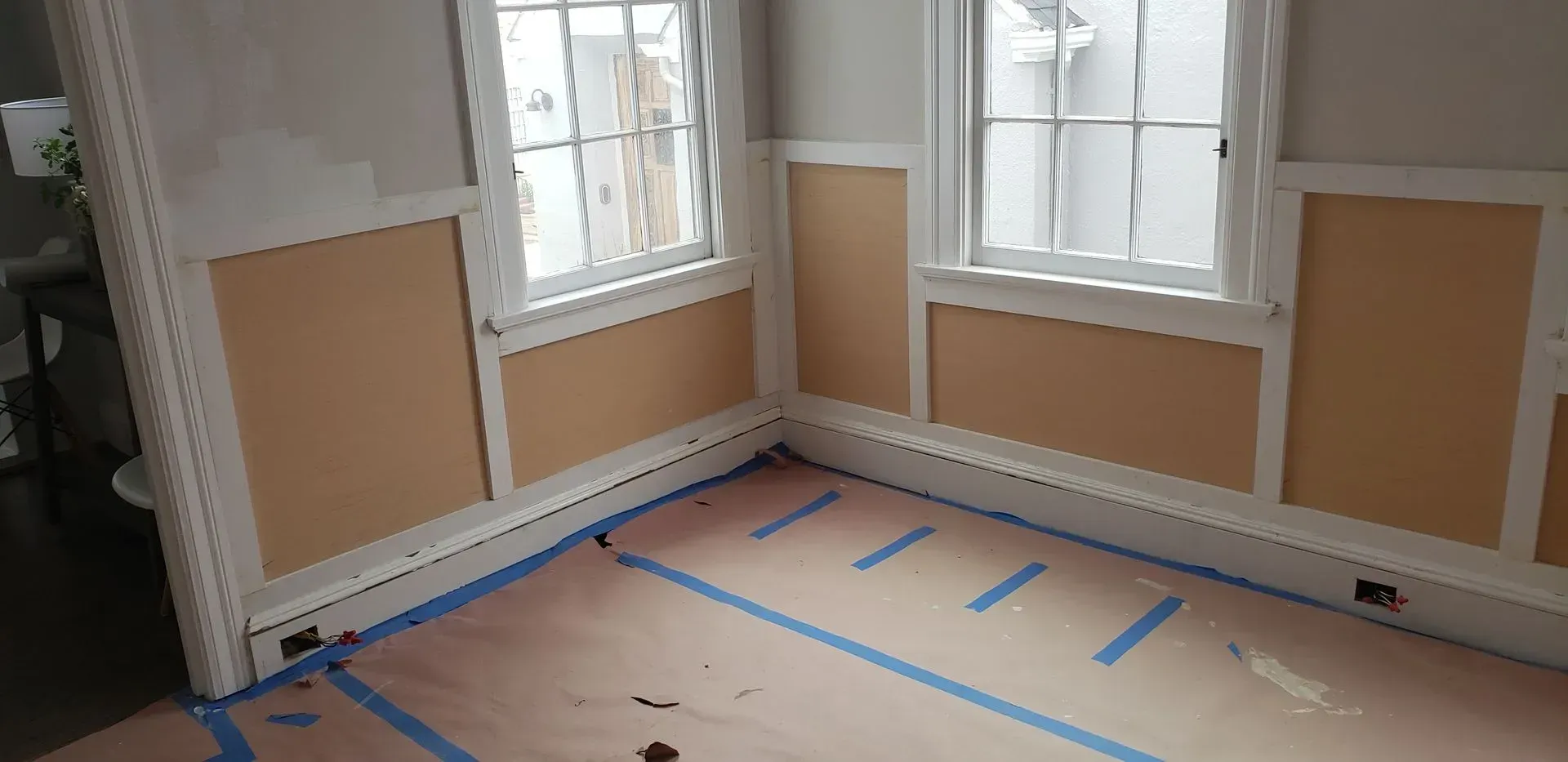 Empty room with windows, beige wall panels, and taped-off flooring under renovation