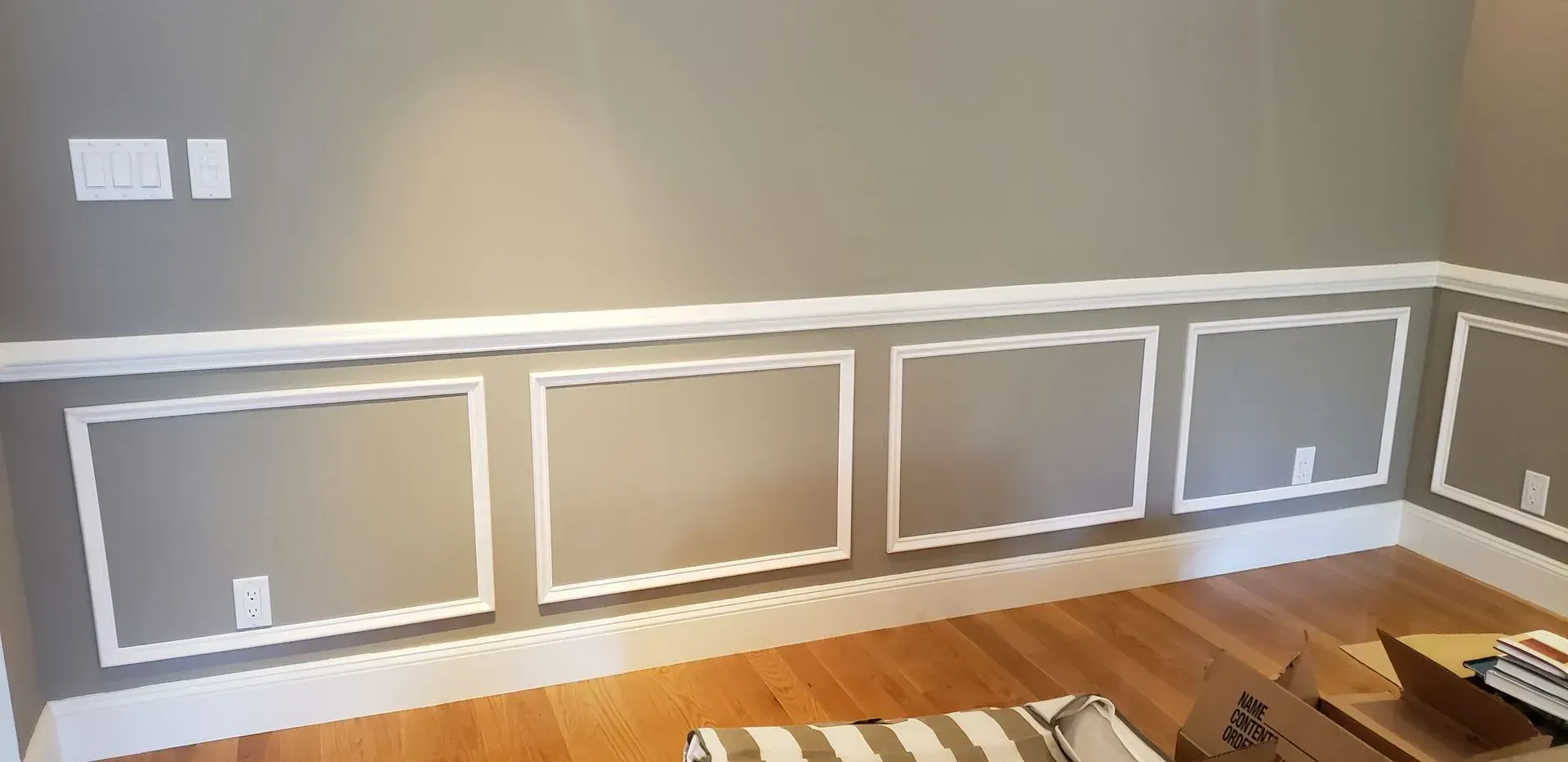 Empty room with white and gray wainscoting, hardwood floor, and a window on the left.