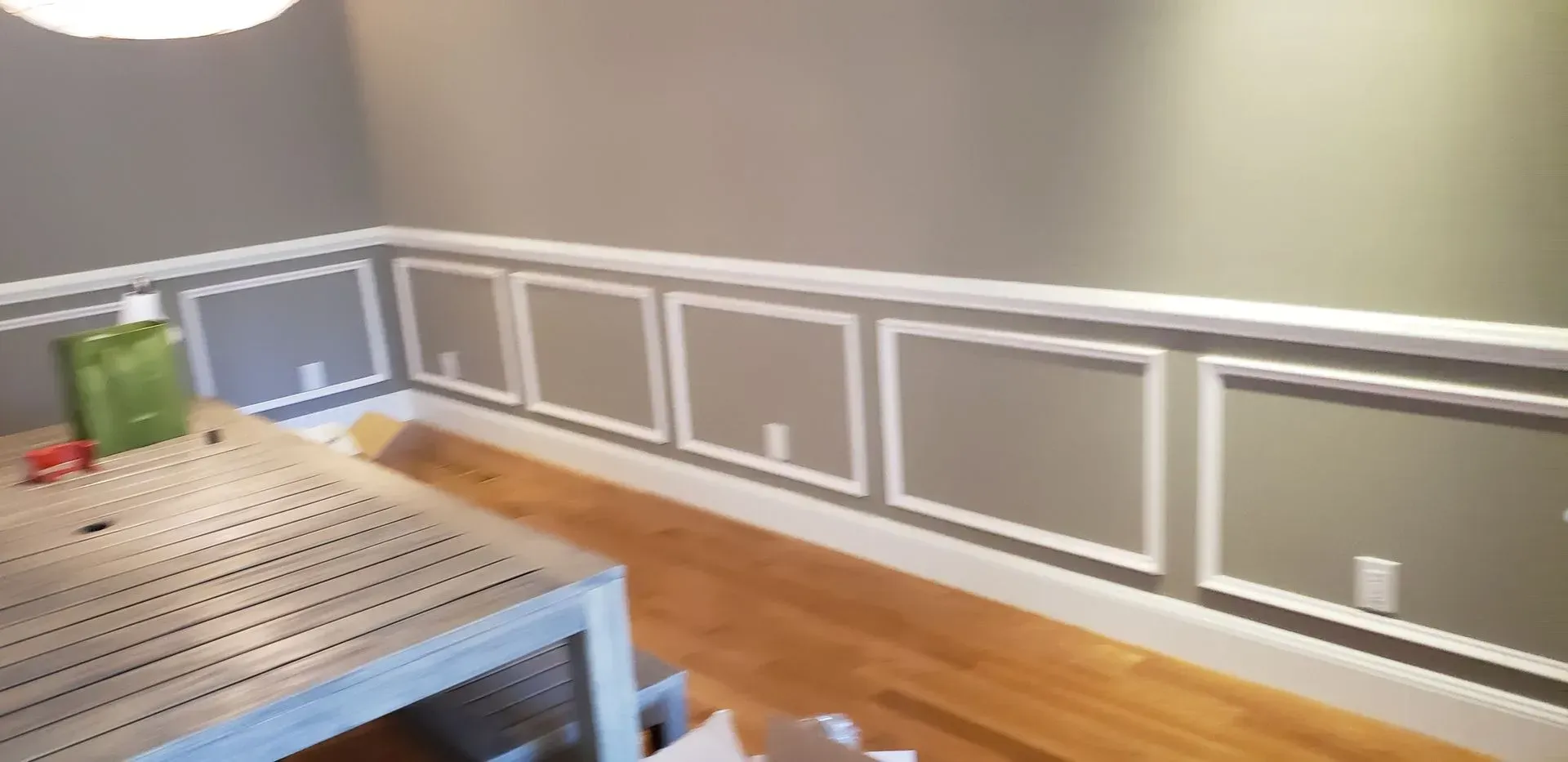 Empty dining room with gray wainscoting, hardwood floors, and a metal table with a green container on it