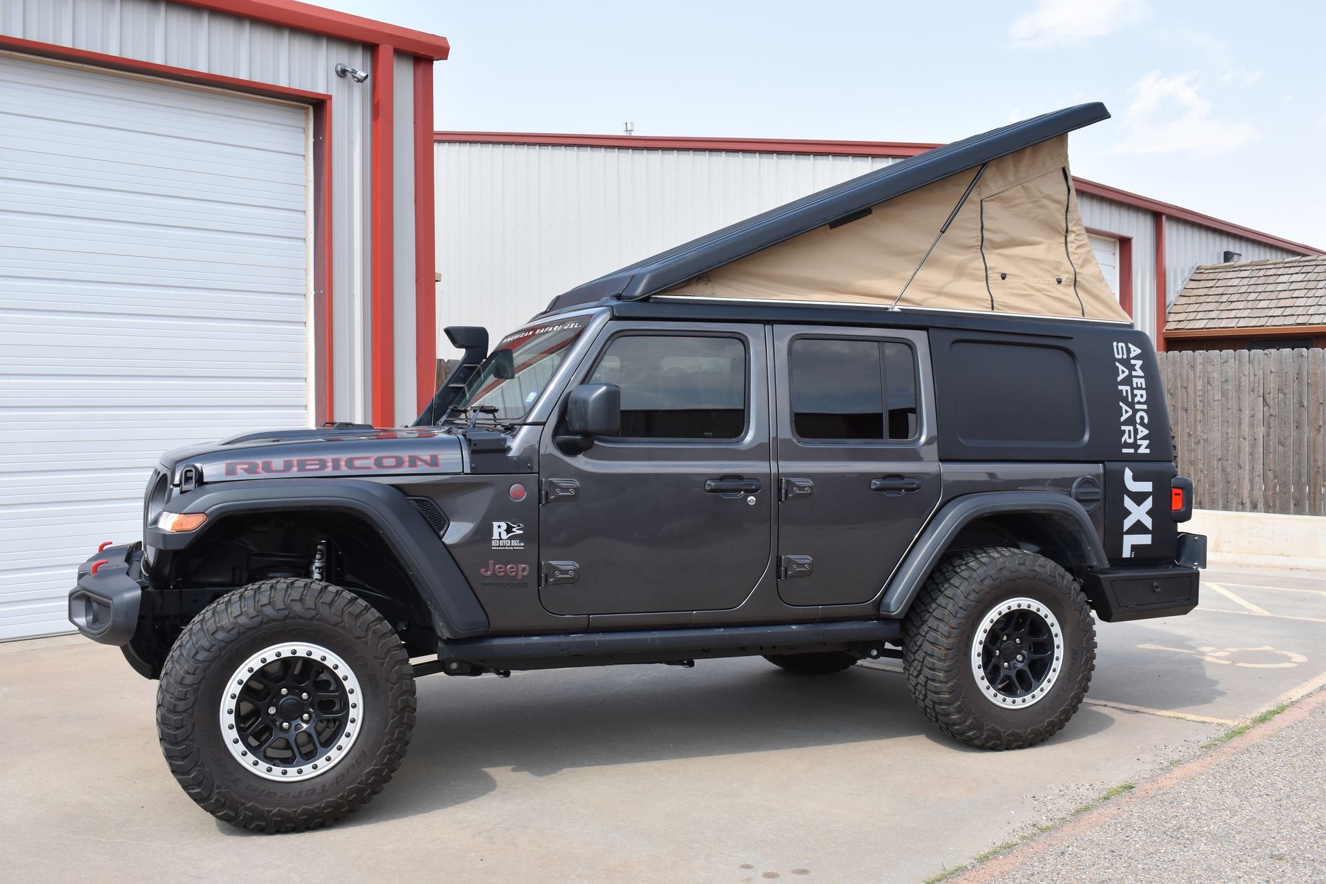 A JXL with the tent popped up is parked in front of a garage.