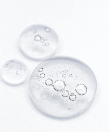 Tre gocce di gel trasparente e viscoso contenenti piccole bolle d'aria, su uno sfondo bianco brillante e uniforme.