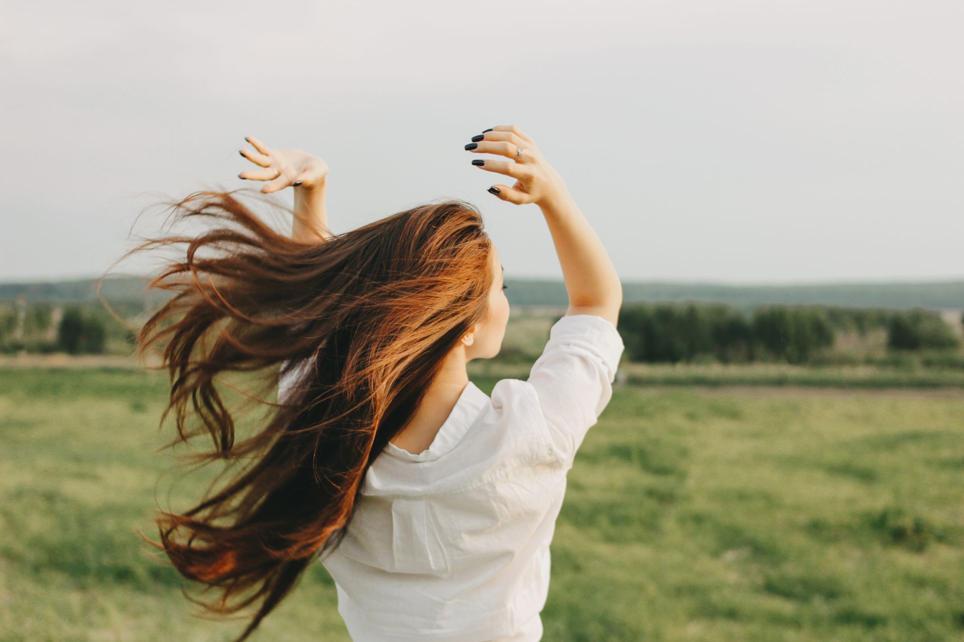Una persona con lunghi capelli fluenti che si protendono verso il cielo in un campo erboso durante l'ora d'oro.