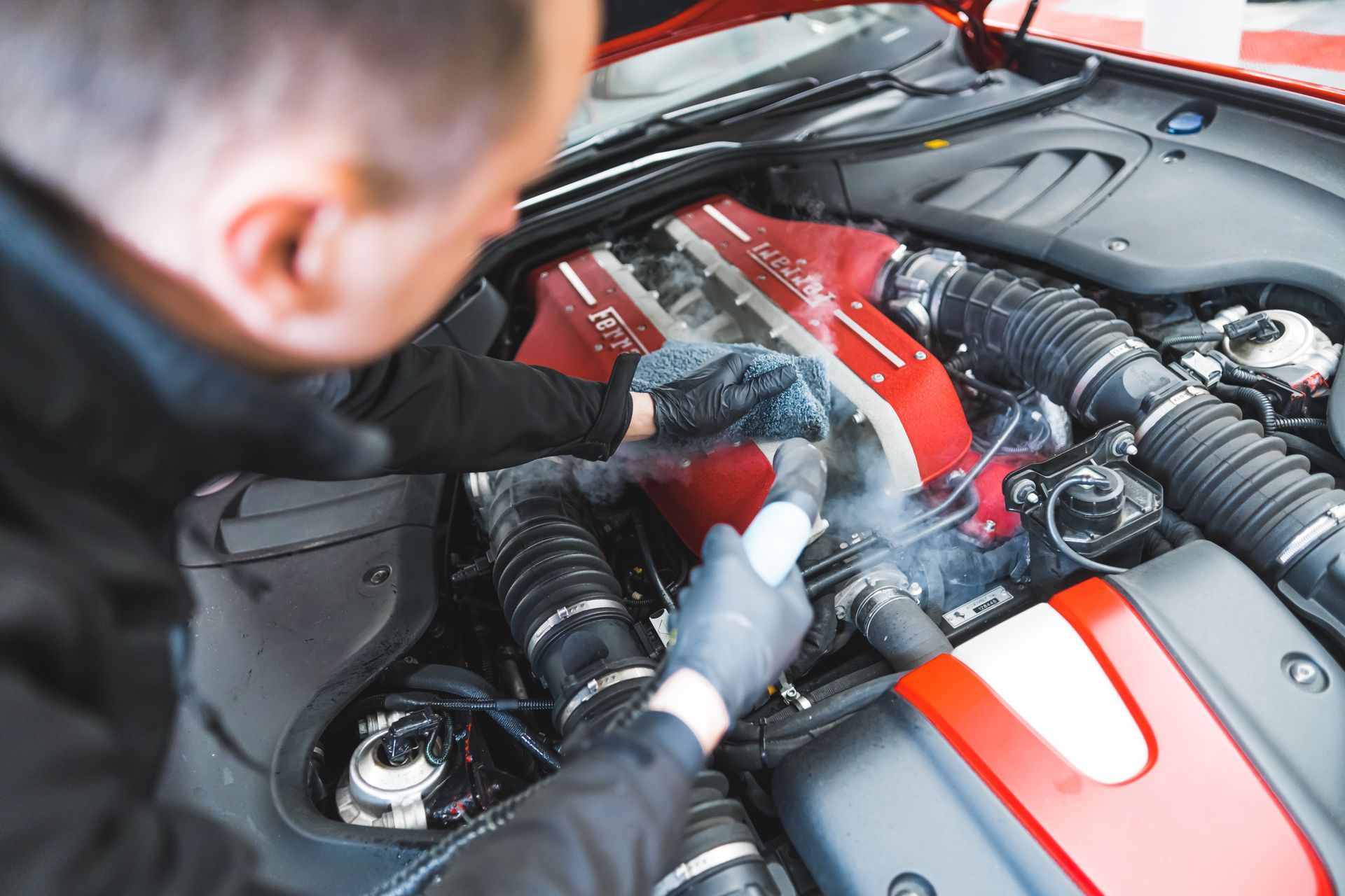 A person wearing gloves steam cleans the red engine bay of a car. A person wearing gloves steam cleans the red engine bay of a car.