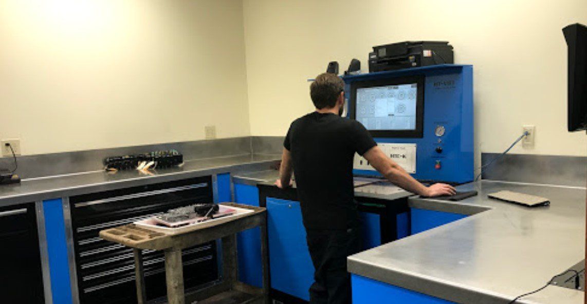 Man working on a machine in a garage-like setting with computer and tools; blue and silver counters.