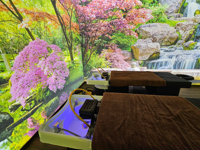 Due lettini per massaggi con asciugamani marroni di fronte a una cascata panoramica e a un murale raffigurante un albero in fiore.