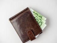 Eine braune Ledergeldbörse mit Geldklammer, die mehrere 100-Euro-Banknoten enthält, isoliert auf weißem Hintergrund.