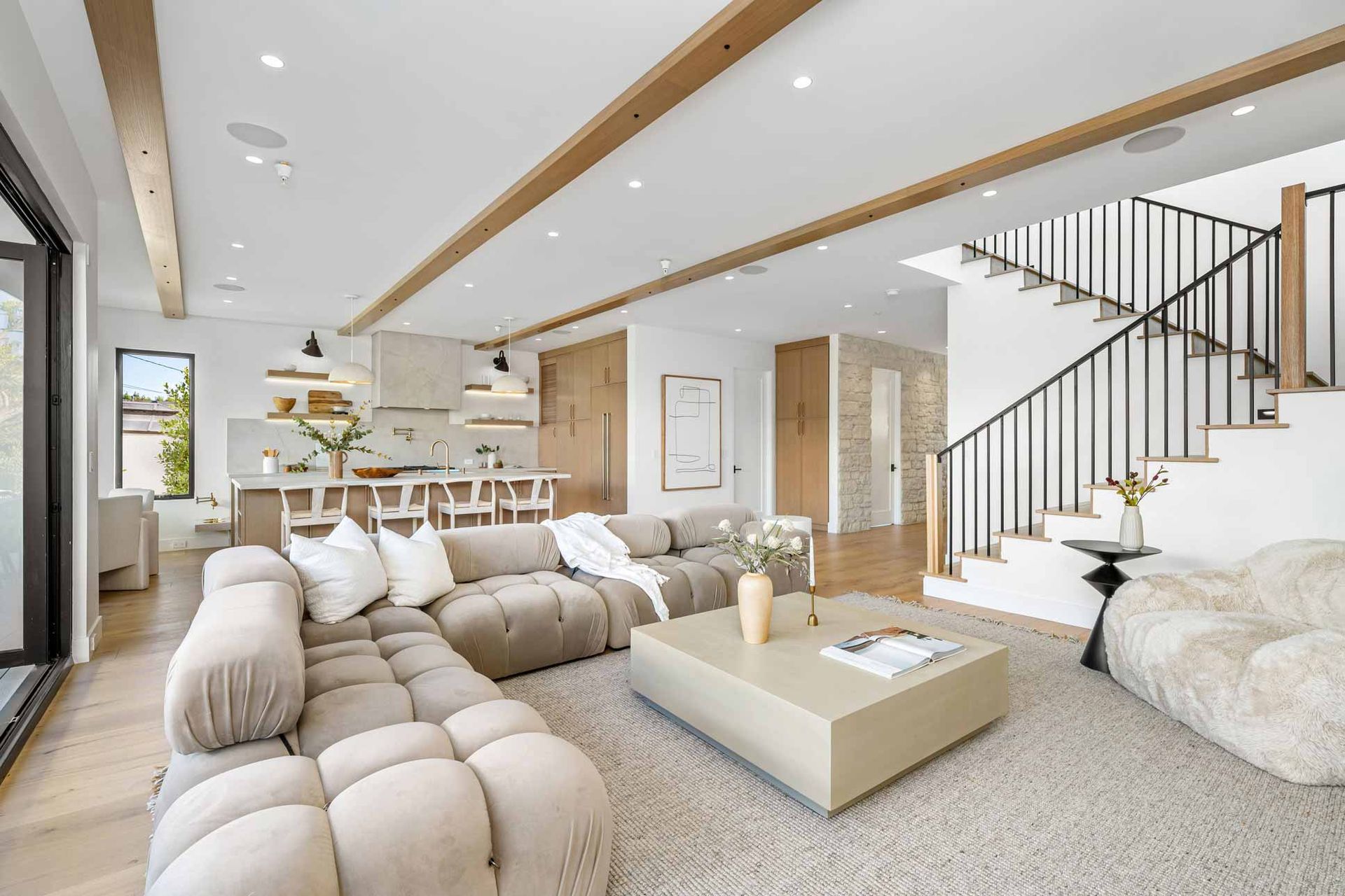 Bright modern living room with beige seating, white rug, and a staircase on the right