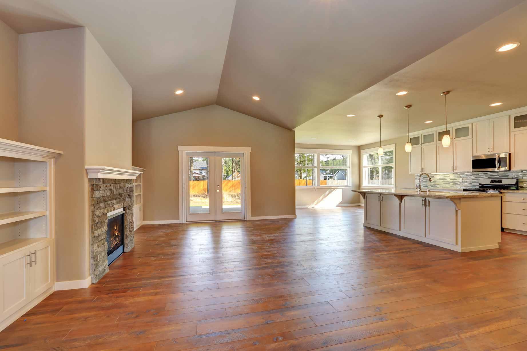 Open-concept living room and kitchen with hardwood floors, vaulted ceiling, and bright natural light