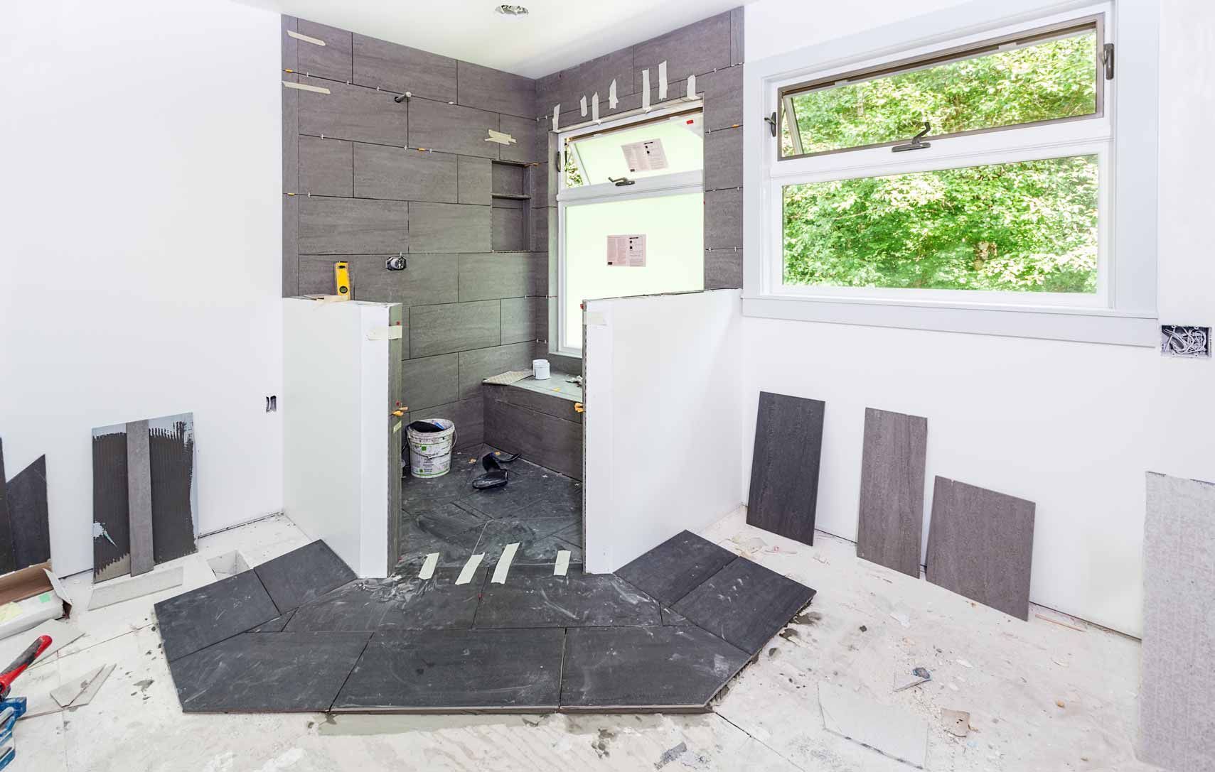 Renovation work in a bright room with gray tile, white walls, and exposed shower plumbing