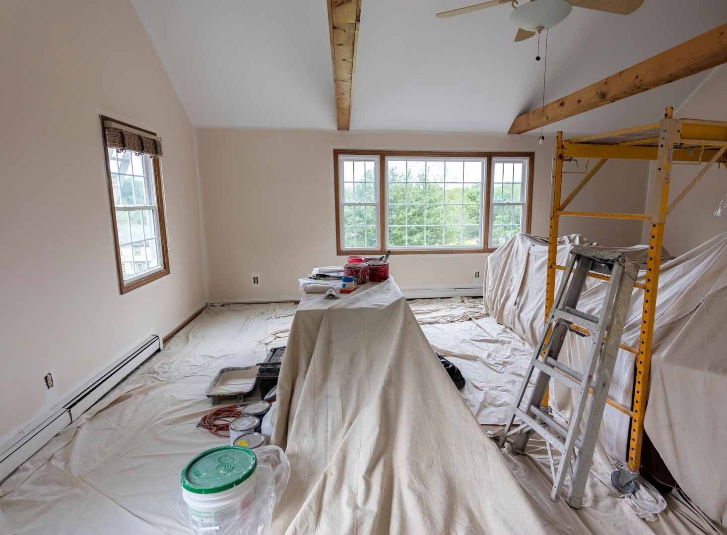 Partially renovated room with tarps, ladder, and tools, lit by a window at the far end