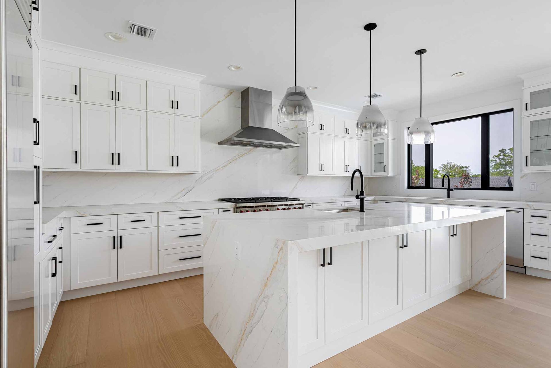 Bright modern white kitchen with island, pendant lights, wood floors, and large windows