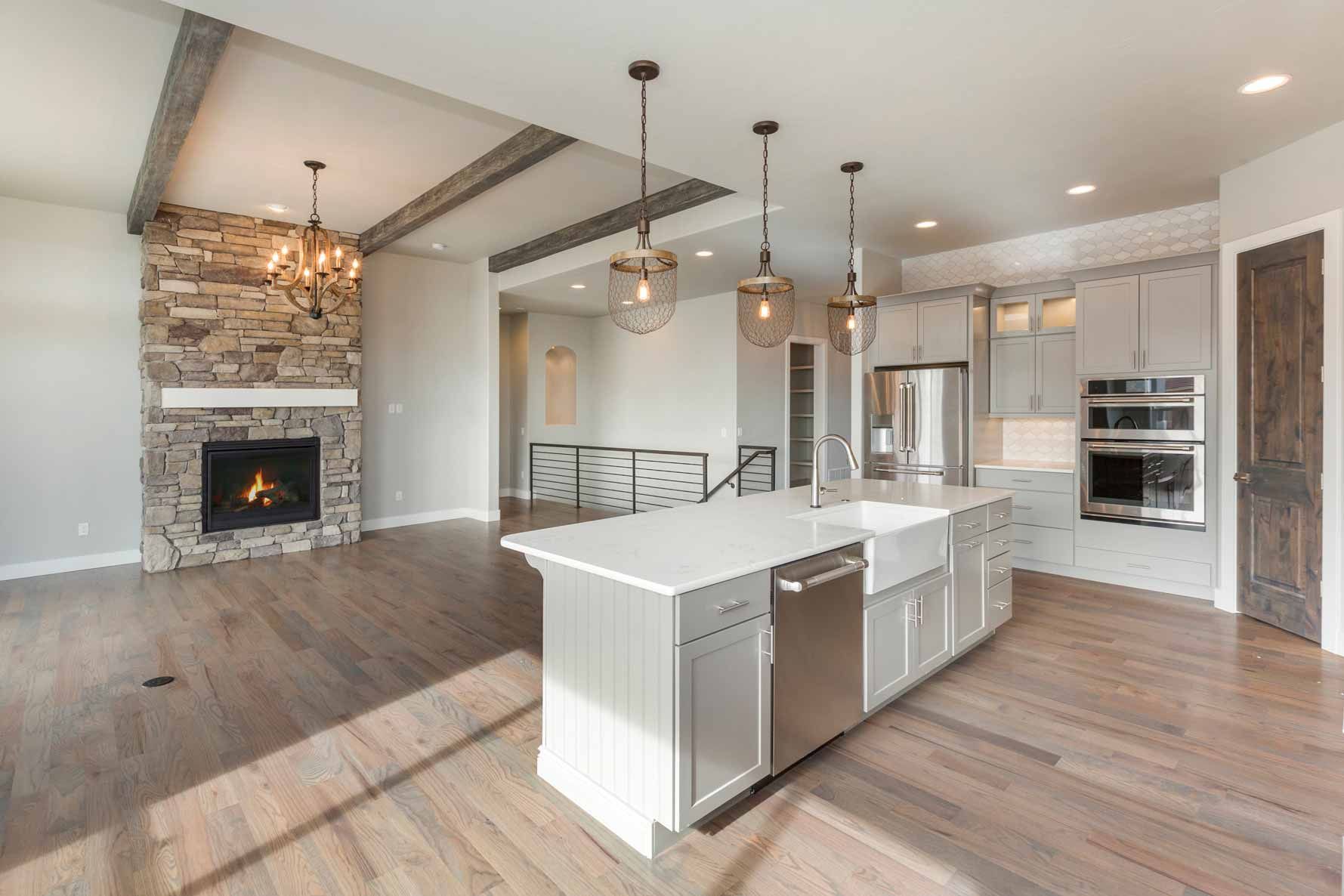 Bright open kitchen and living area with white island, pendant lights, hardwood floors, and stone fireplace