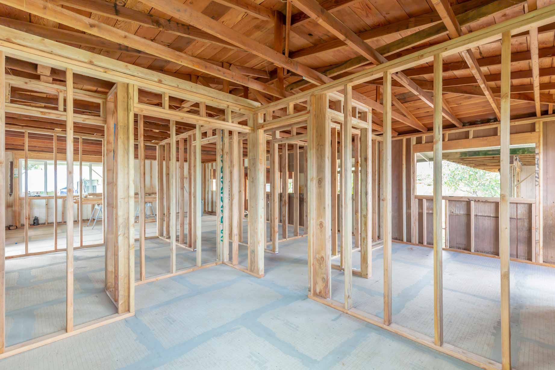 Unfinished house interior with exposed wooden framing and plywood subfloor.