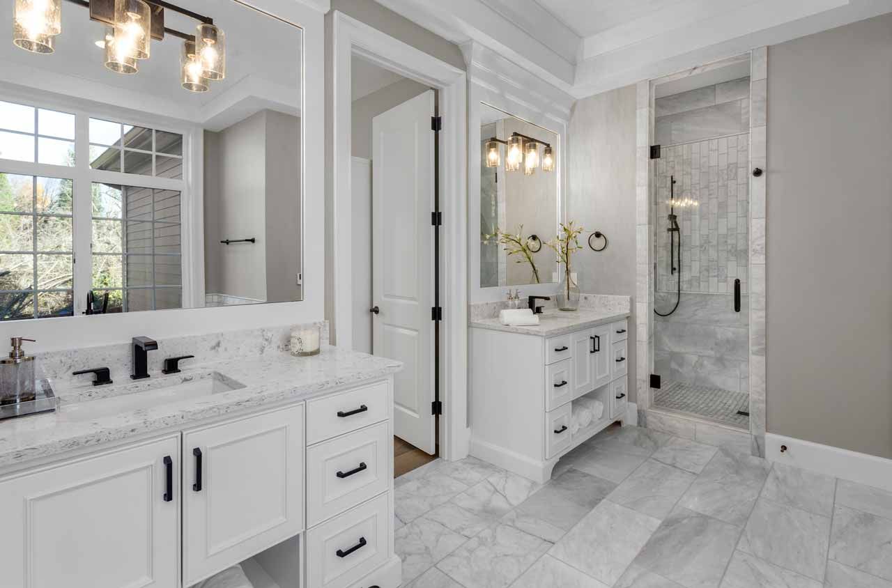 Bright white marble bathroom with double vanity, large mirrors, and glass shower.