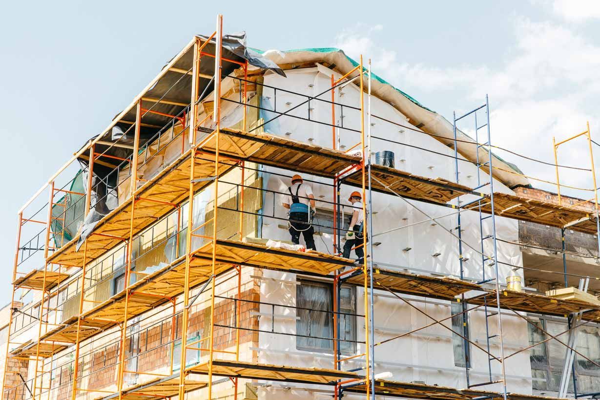 Workers on scaffolding around a building under construction with orange safety netting.