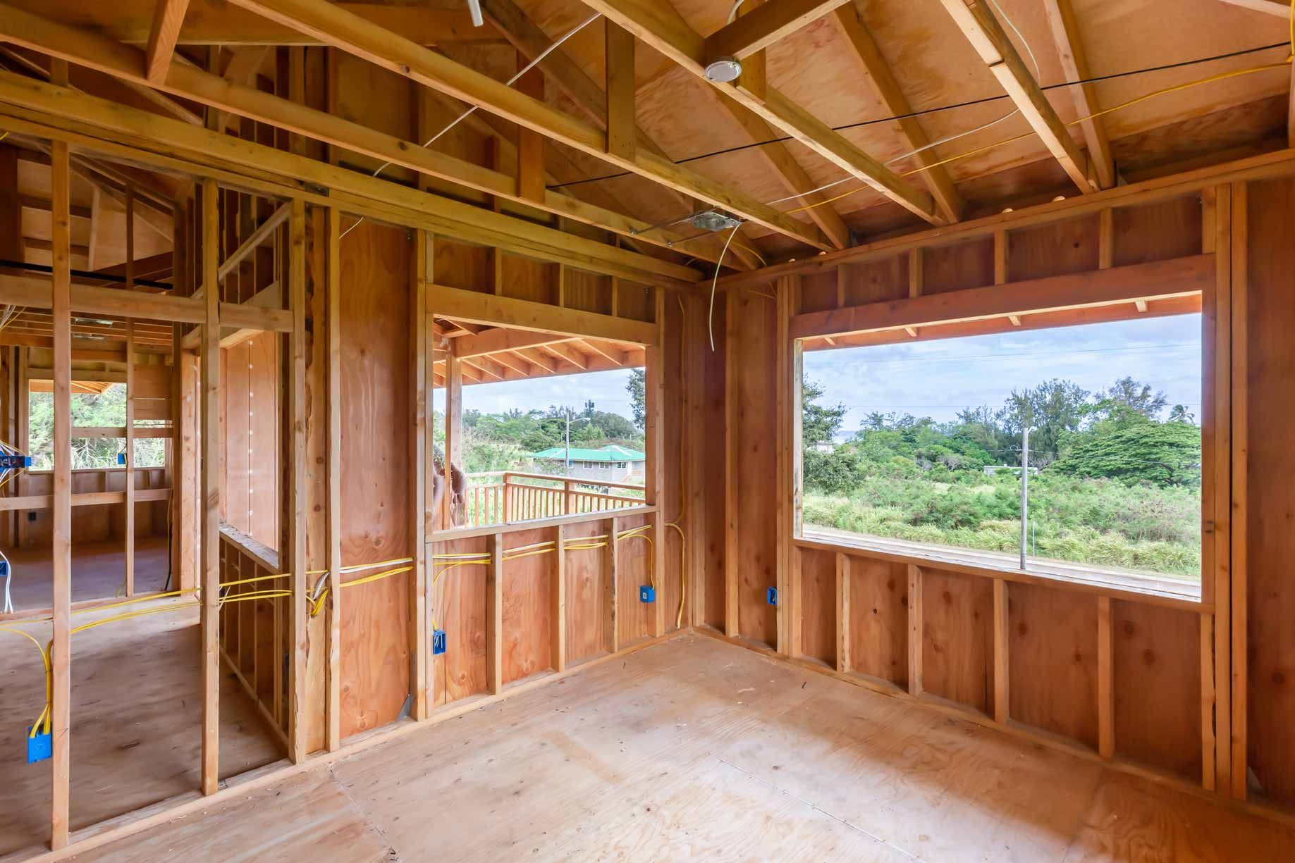Unfinished wooden house interior with exposed framing, open windows, and a view of greenery outside