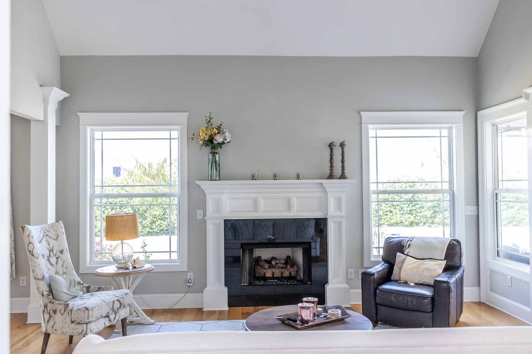 Bright living room with white fireplace, two windows, patterned armchair, and gray accent chair.