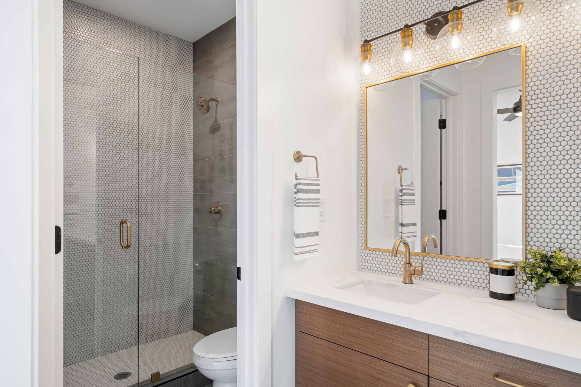 Modern bathroom vanity with lit mirror and tiled shower stall in the background