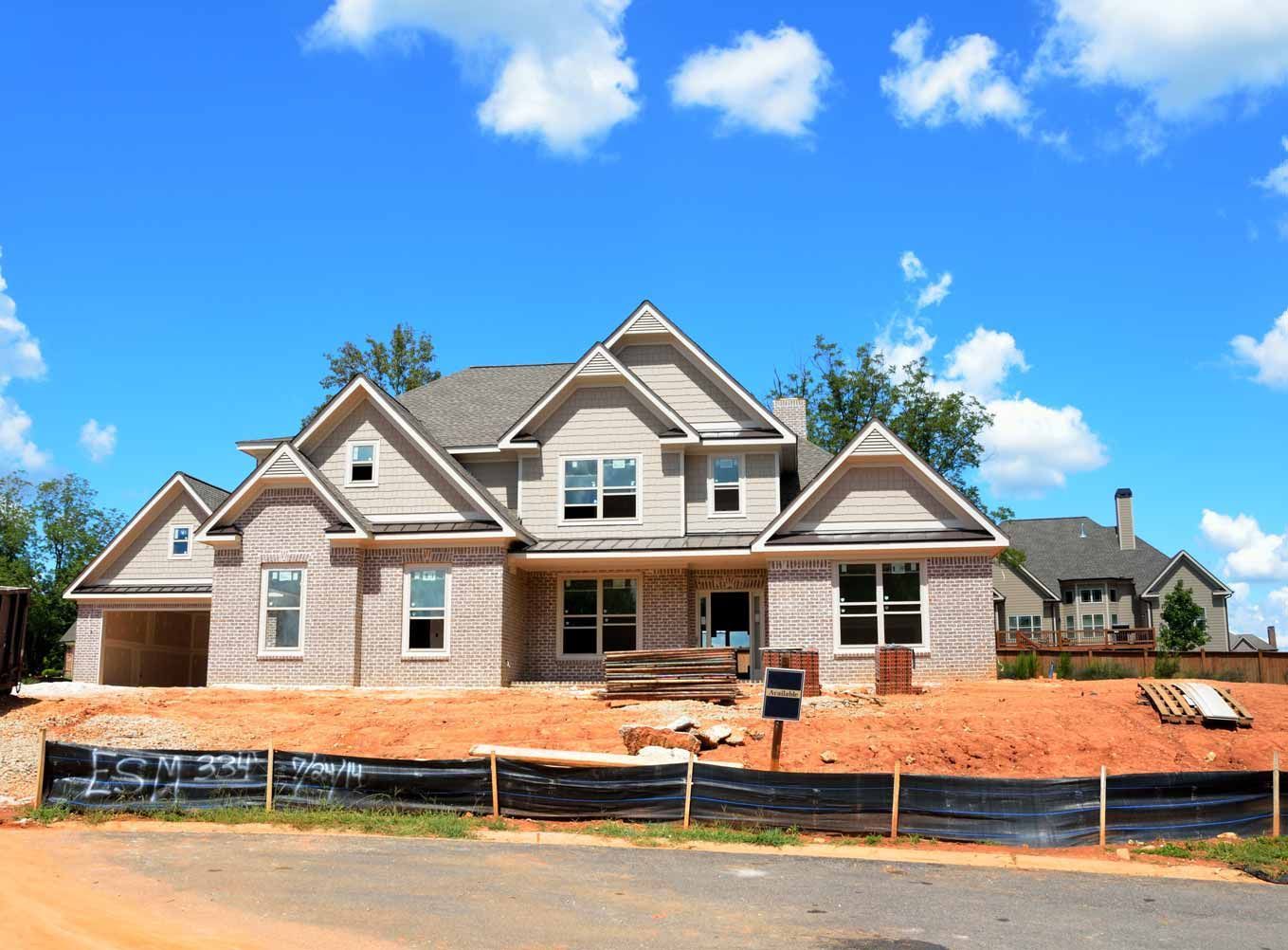New house under construction with brick and wood framing, blue sky, and dirt lot in front