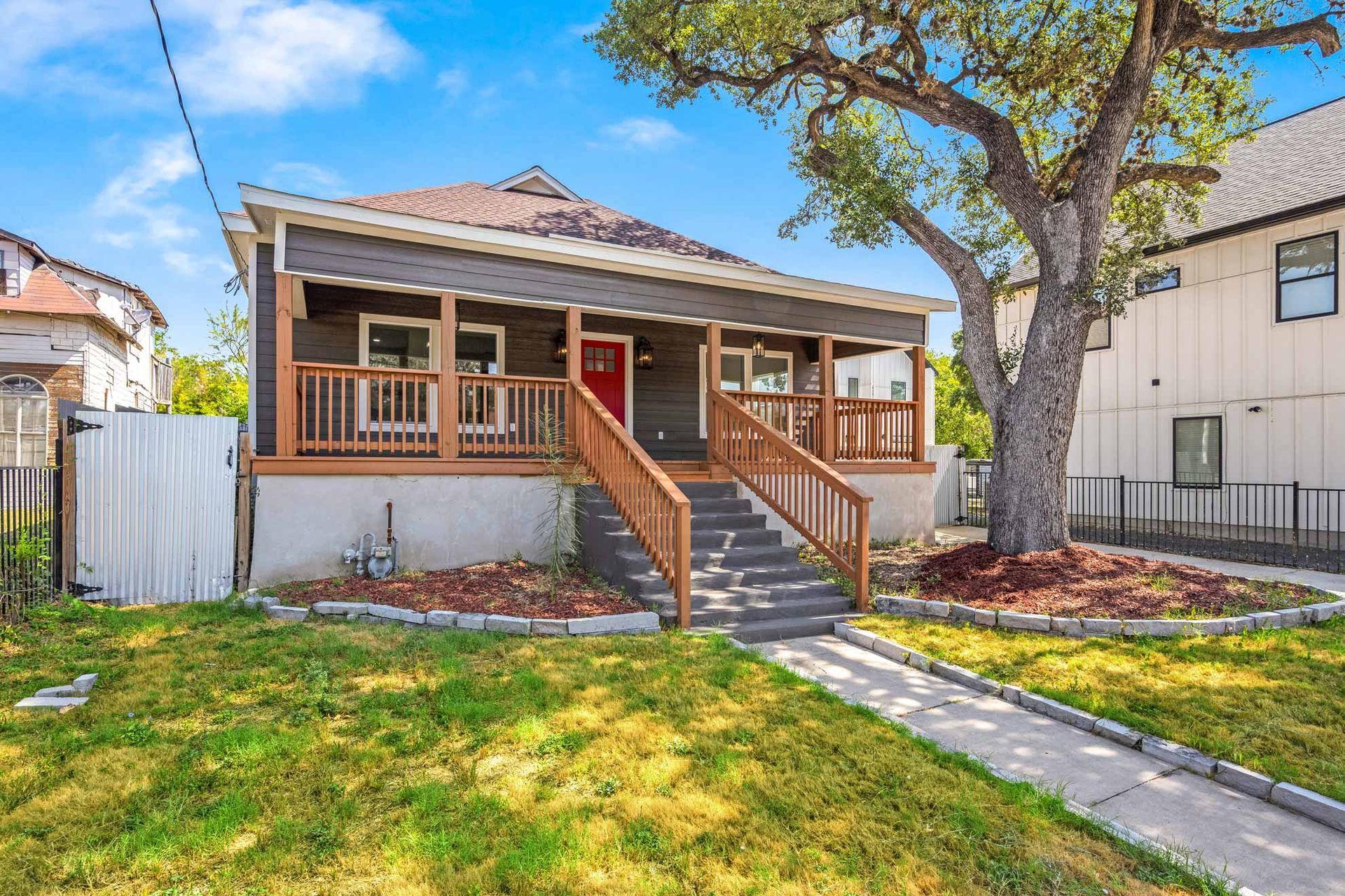 Front porch bungalow with red door, stairs, and a green front yard on a sunny day